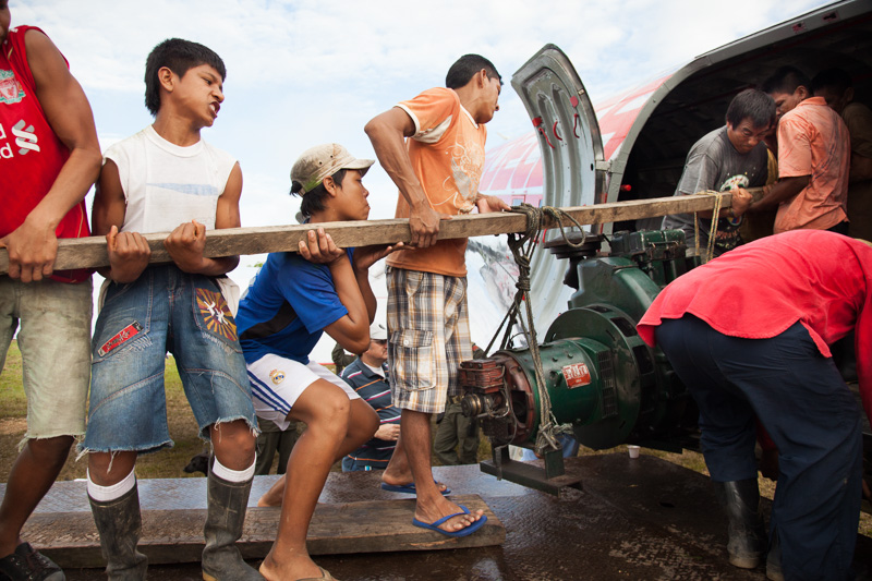 Photo Young indigenous men struggle to hoist a broken engine onto a DC-3 plane in the remote jungle village of La Pedrera, Amazonas. 